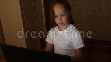 女孩晚上在用笔记本电脑读电子书。 儿童坐在社交网络的电脑和检查电子邮件